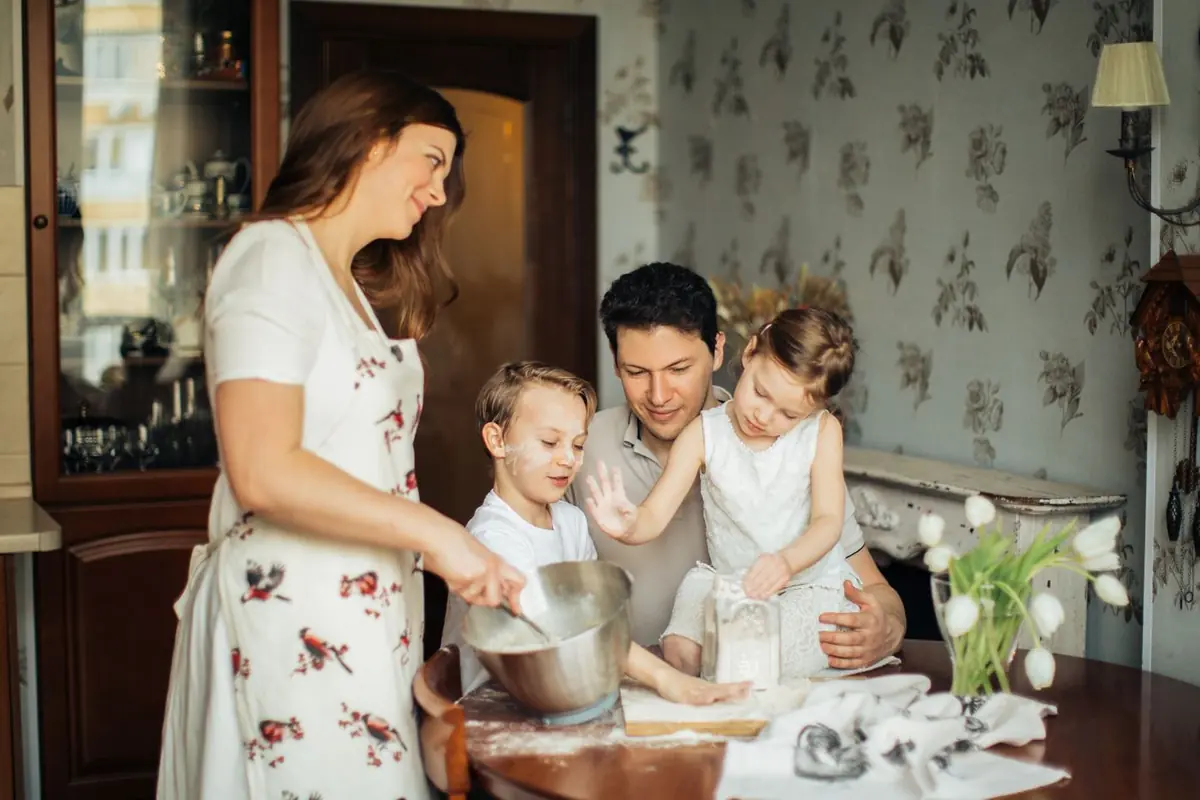 Eltern und Kinder backen gemeinsam am Küchentisch und bereiten Essen zu.